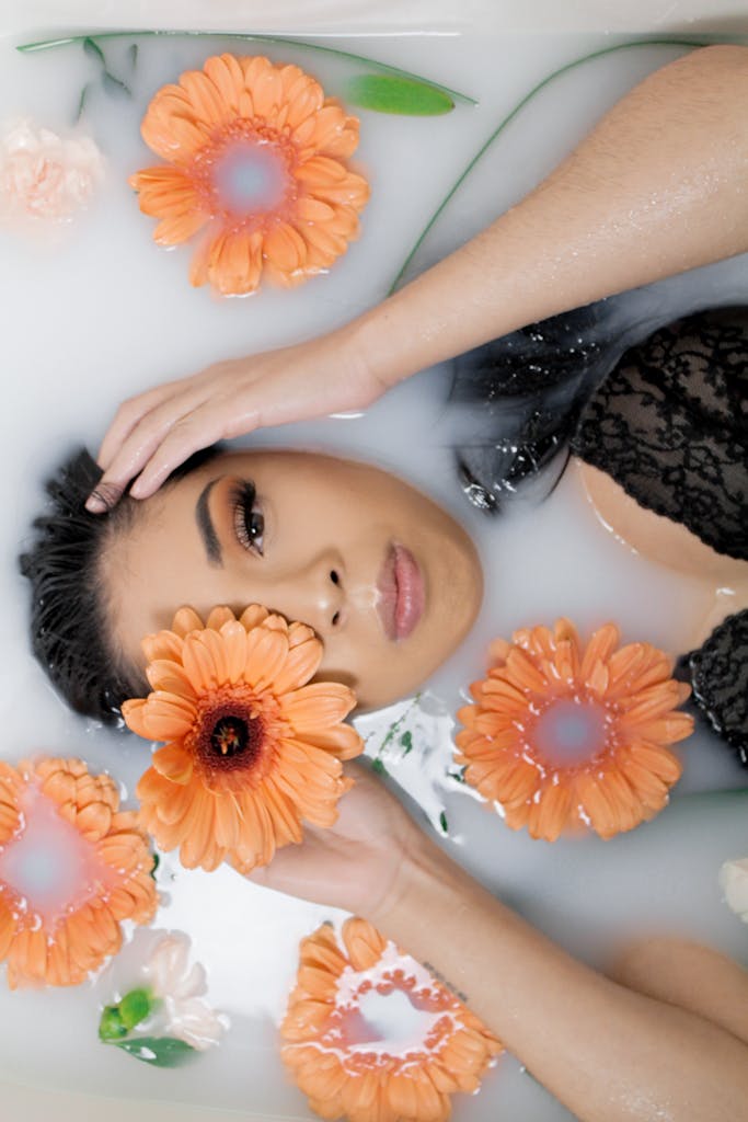 Woman in a black lace top relaxing in a milk bath with orange flowers. bağlıca cilt bakimi